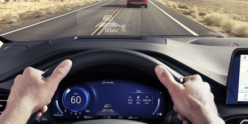 POV shot of hands on a steering wheel, showing the digital instrument cluster and a heads-up display with speed and a vehicle graphic