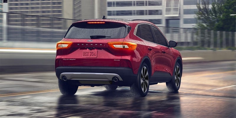 A rear view of a red Ford Escape Platinum SUV driving on a wet city street