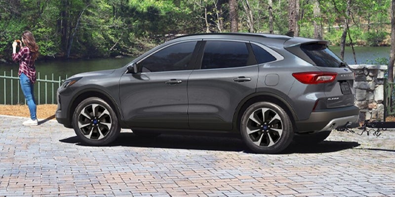 A grey Ford Escape SUV is parked on a paved driveway with a woman standing nearby